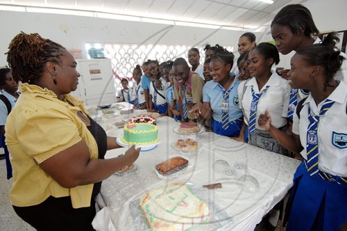 Ian Allen/Staff Photographer
Elsa Codling, left, Food and Nutrition teacher at Papine High School puts the finishing touches to a cake on display at the school's Open Day, under the watchful eyes of student in attendance.