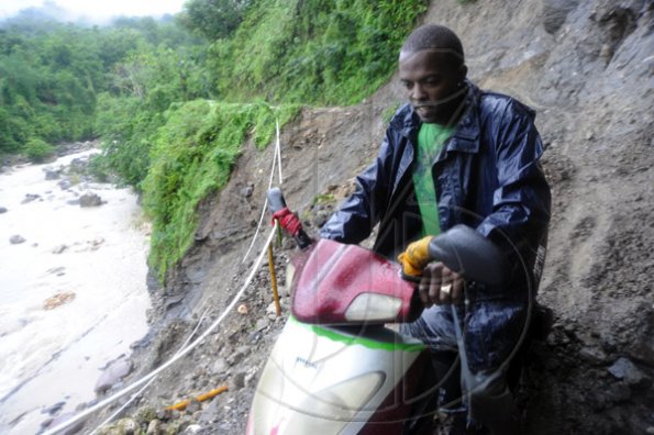Ricardo Makyn/Staff Photographer.
John Beckford dangerously rides His bike along whats left of a embankment at Friday in the  Rio Grande Valley after Rainfall had caused a Landslide that totally destroyed what was left of the roadway .