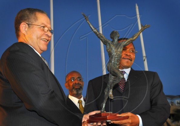 Prime Minister Bruce Golding presents Tanzania President Jakaya Mrisho Kikwete, with a miniature statue at the unveiling of the Herb McKenley monument. Basil Watson, the artist that created the sculptures, watches from behind the nation leaders.
