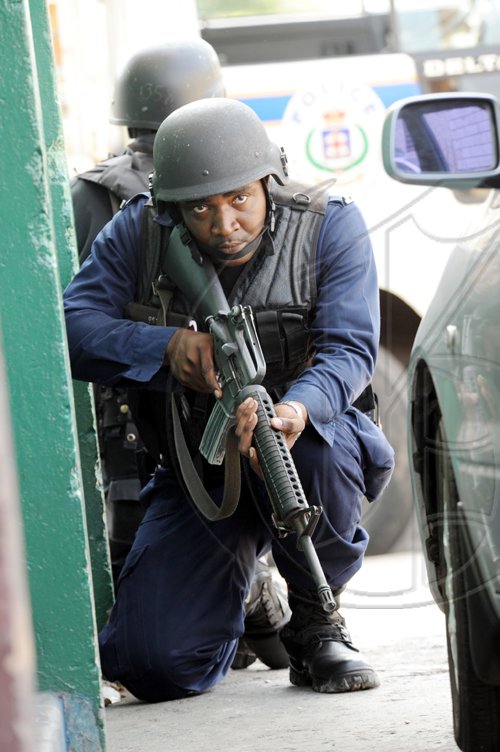 Norman Grindley /Chief Photographer
A policeman takes cover behind a vehicle as lawmen and gunmen in the Hannah Town area of West Kingston yesterday.